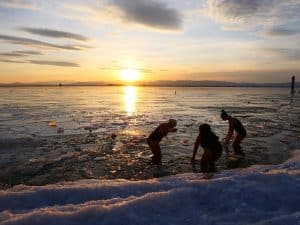 Three women standing in a lake, moving ice out of the way to wade in the frigid water