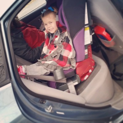 Flor, at 3.5 years old, can be seen here strapped into her car seat (still facing backwards), staying warm wearing a poncho over her seat straps.