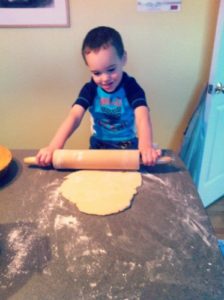 child rolling out dough after interrupting his mom.