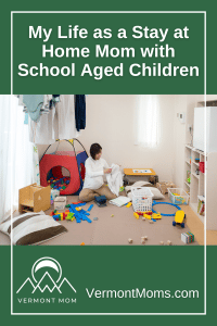 This is a pinnable image for a blog post about being a stay at home mom to school aged children. It features the title of the blog post and an image of a mom folding laundry in a messy play room.