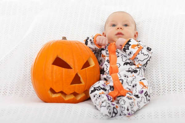 baby in a Halloween onesie next to a jack'o'lantern