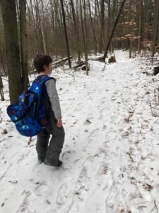 A boy walking in the woods wearing a blue backpack