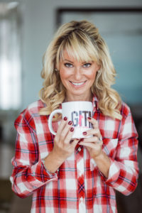 blond woman wearing red plaid shirt holding coffee mug.