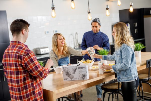 two men and two women share boxed drinks over a kitchen island