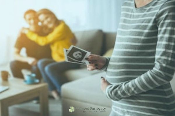 pregnant person holding belly with a couple embracing in the background