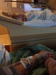 Image of infant swaddled in hospital bassinet with mother's arm with IV in foreground.