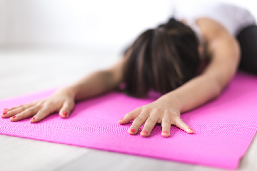 A woman is bent over in child's pose on a pink yoga mat.