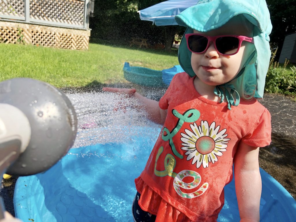 A toddler is wearing a blue hat, swinging on a yellow swing. The chains and poles of the swing set frame her.