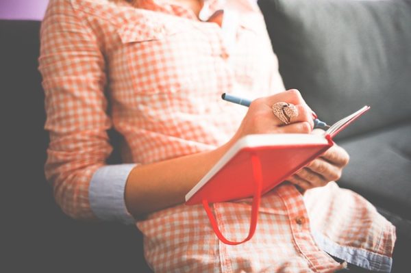 female in checked shirt writing in a journal