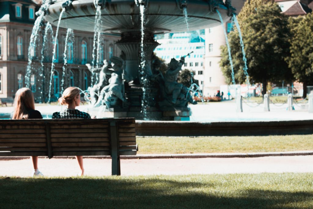 2 women on a bench in front of a fountain
