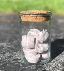 a glass jar is on the ground holding bath bombs