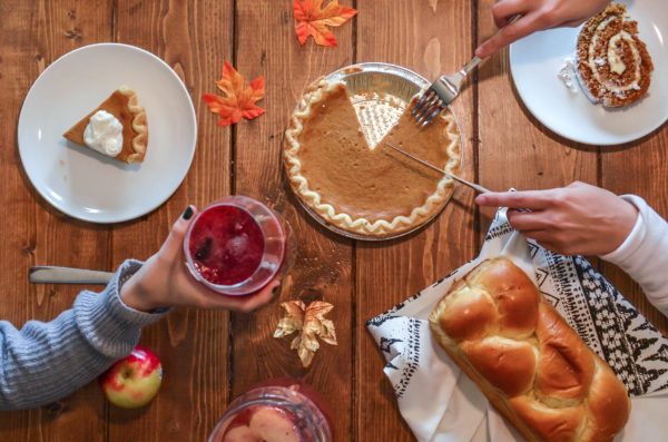 hands cutting pumpkin pie and holding a red drink.