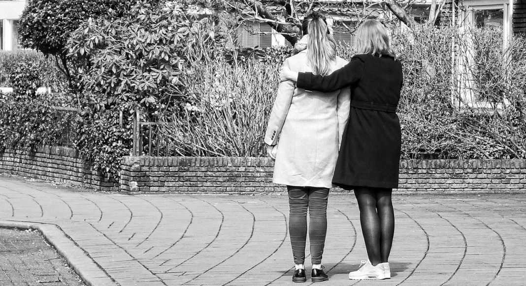 I’m Not Okay, but Don’t Ask Me About It: Finding Strength in Vulnerability A black and white image of two women facing away from the camera, with one with her arms around the other