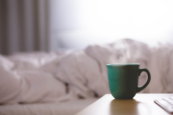 green coffee mug with a cozy bed in the background