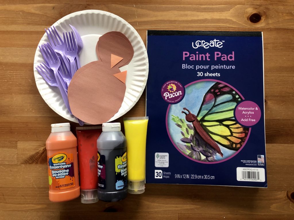 Viewed from above are a pad of paper, finger paints, paper plate, plastic forks, and construction paper cut-outs.