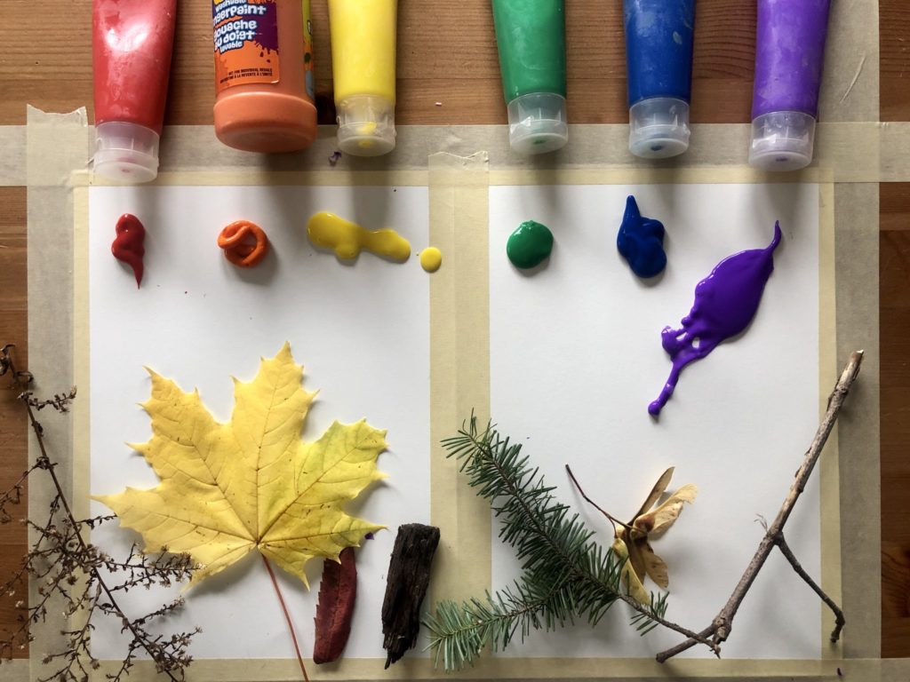 Viewed from above are collected natural objects and an array of finger-paints on top of white paper.
