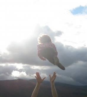 hands tossing a child up into the sky