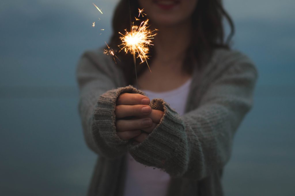 A woman holds up a lit sparkler to the camera