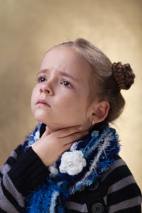 Girl wearing scarf and striped sweater holding her throat in pain