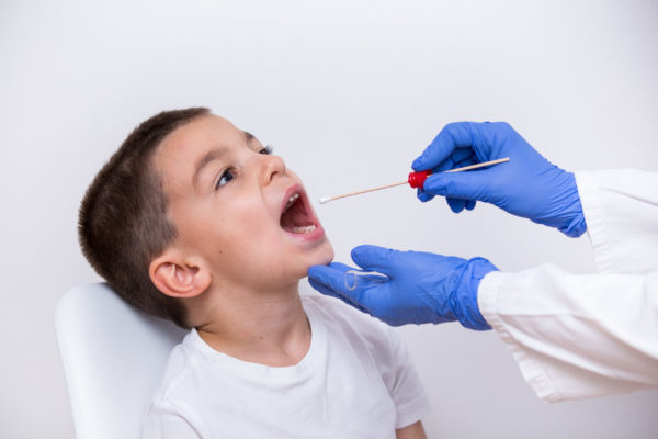 Boy in white gets throat swabbed by medical provider wearing blue gloves