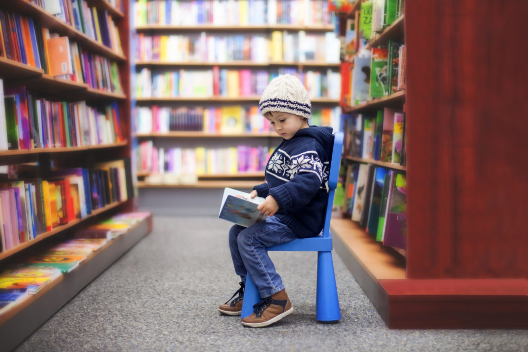 You Belong at Your Public Library Plus 5 More Reasons to Visit little boy on plastic chair in the aisle of a public library