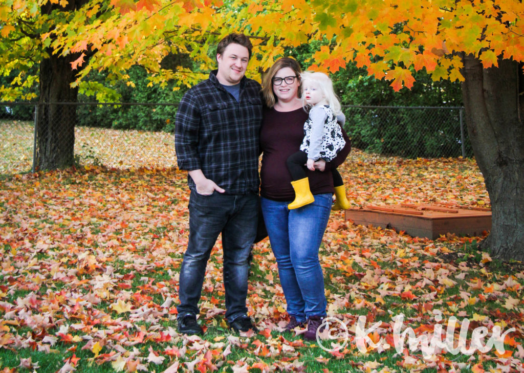 A family portrait of a husband, wife, and toddler daughter in autumn
