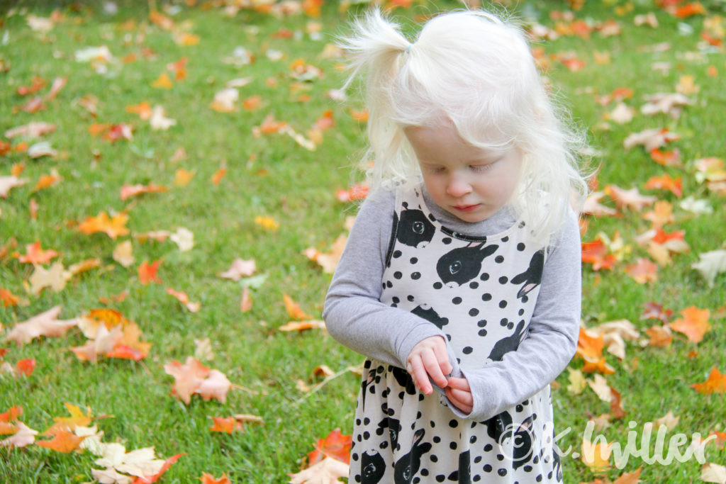 Toddler standing in the leaves, looking at her hands