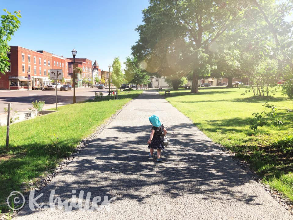 toddler with albinism walking down sidewalk wearing a turquoise sunhat