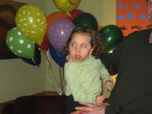 young girl who is medically fragile being supported by a parent and surrounded with balloons