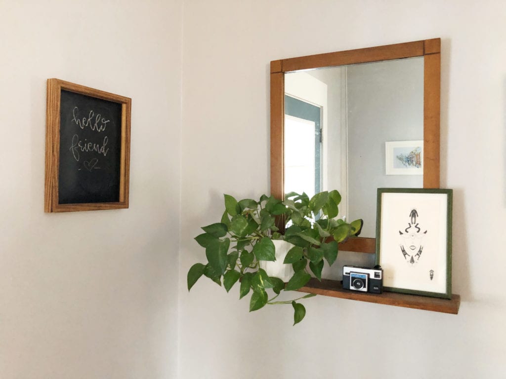 A potted plant on a shelf, with a mirror and some art.