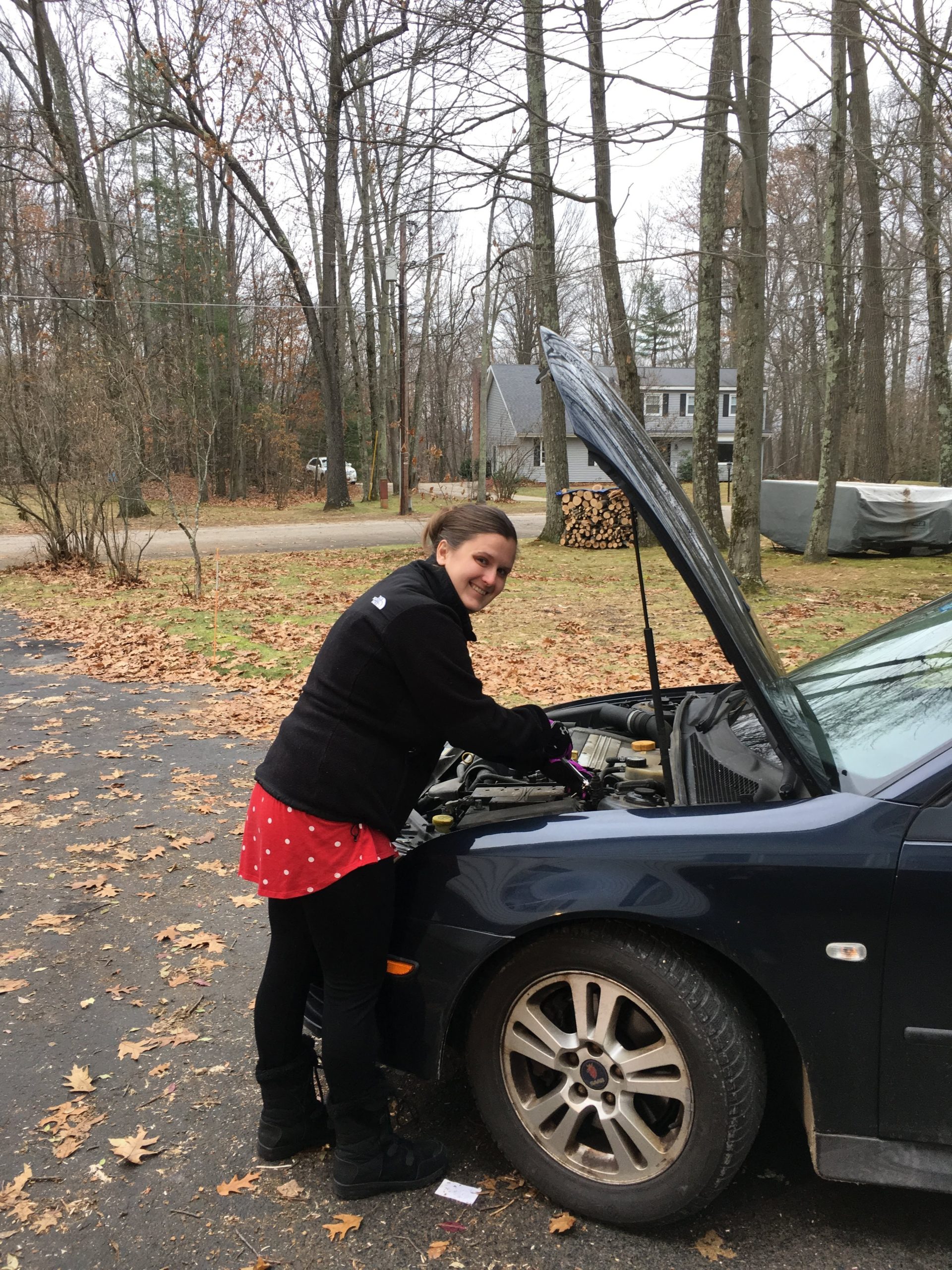 woman performs vehicle maintenance on car engine