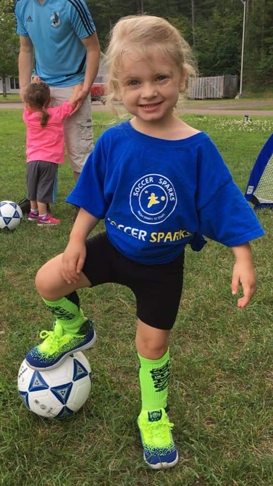 girl playing soccer and posing with a soccer ball.