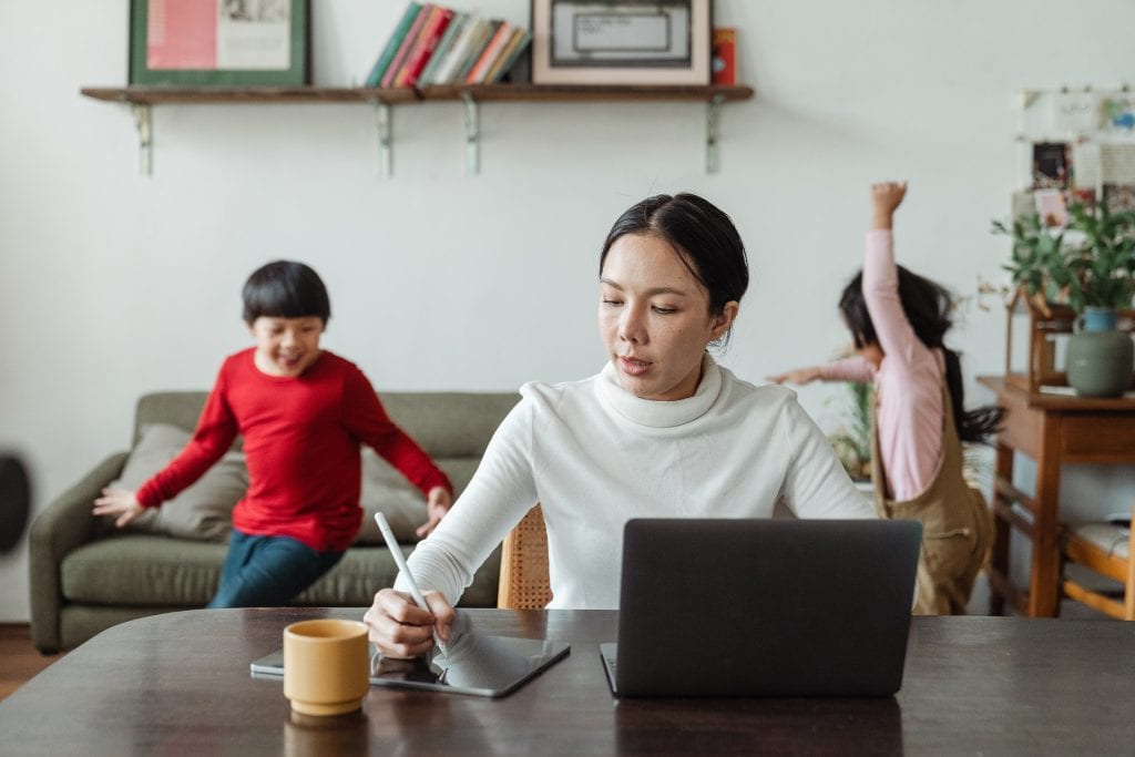 A woman working at a laptop with children behind her