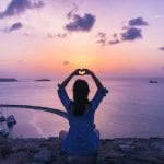 woman-sitting-on-rock-doing-heart-hand-gesture-1399034