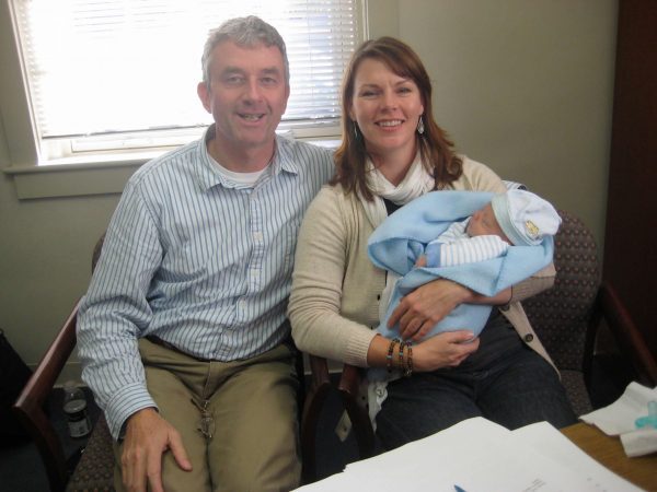 man and woman holding a baby wrapped in blue blankets
