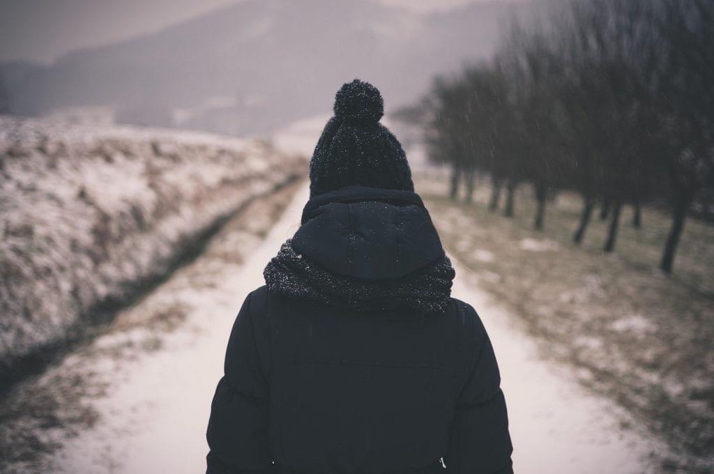 A woman walks a snow path bundled in winter gear