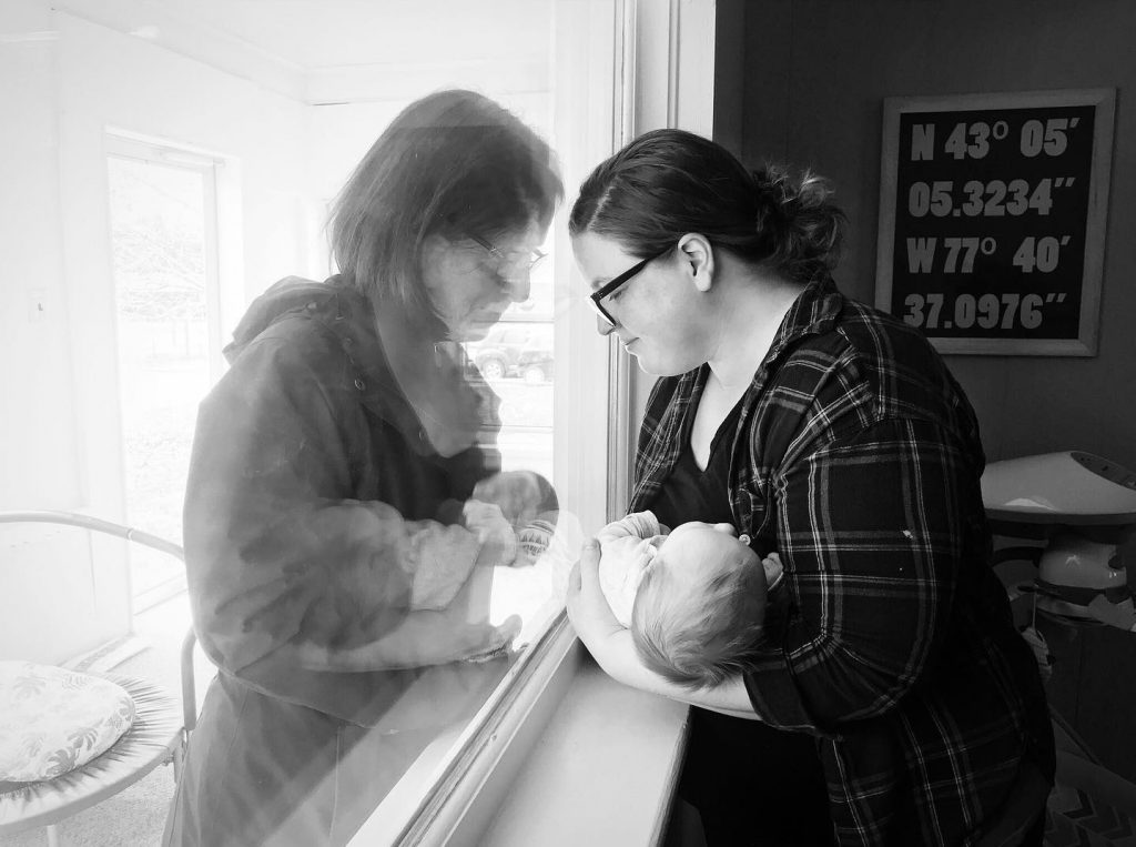 Two women bow their heads together, a pane of glass between them.