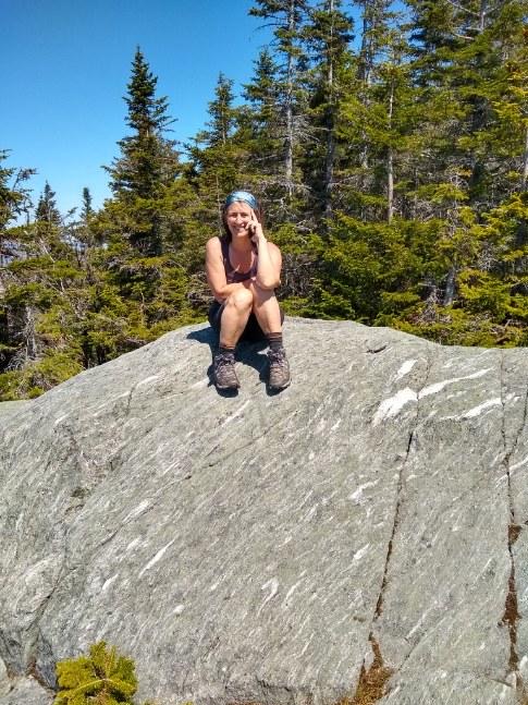 woman sits on a boulder while on a hike