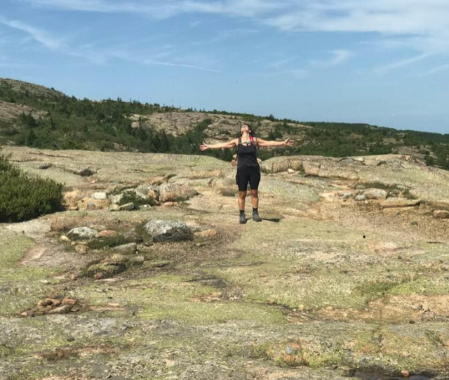 woman with outstretched arms on a rocky summit