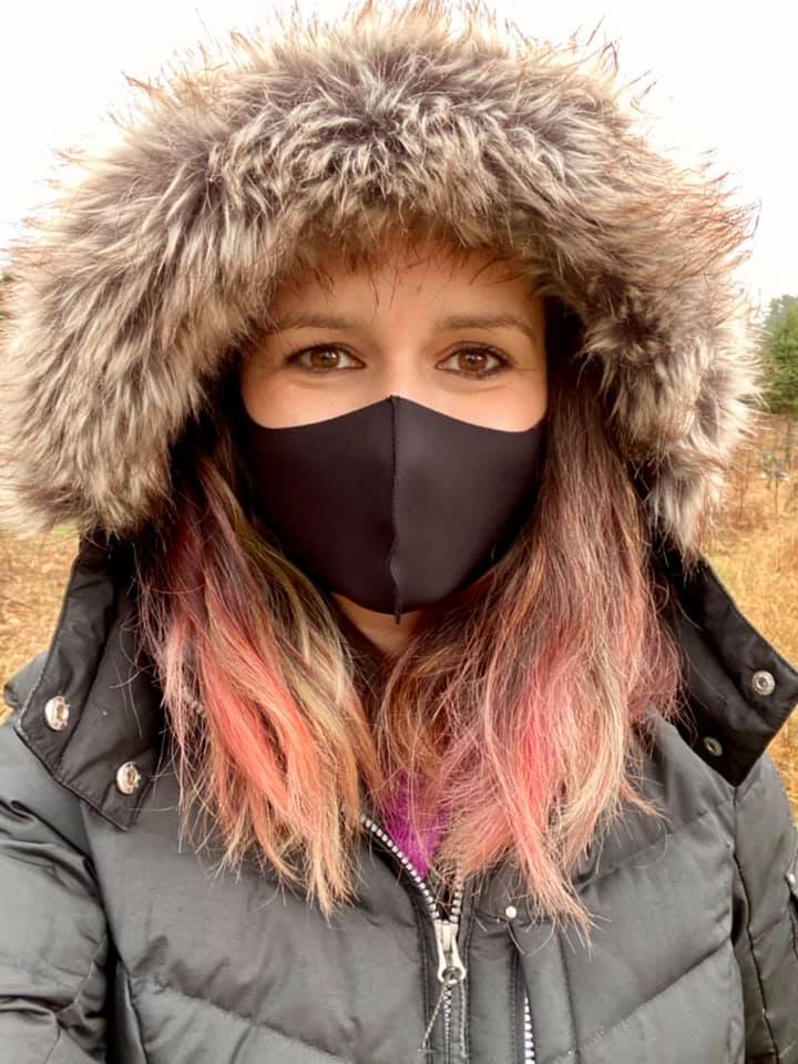 woman in a winter coat with a furry hood, wearing a covid mask