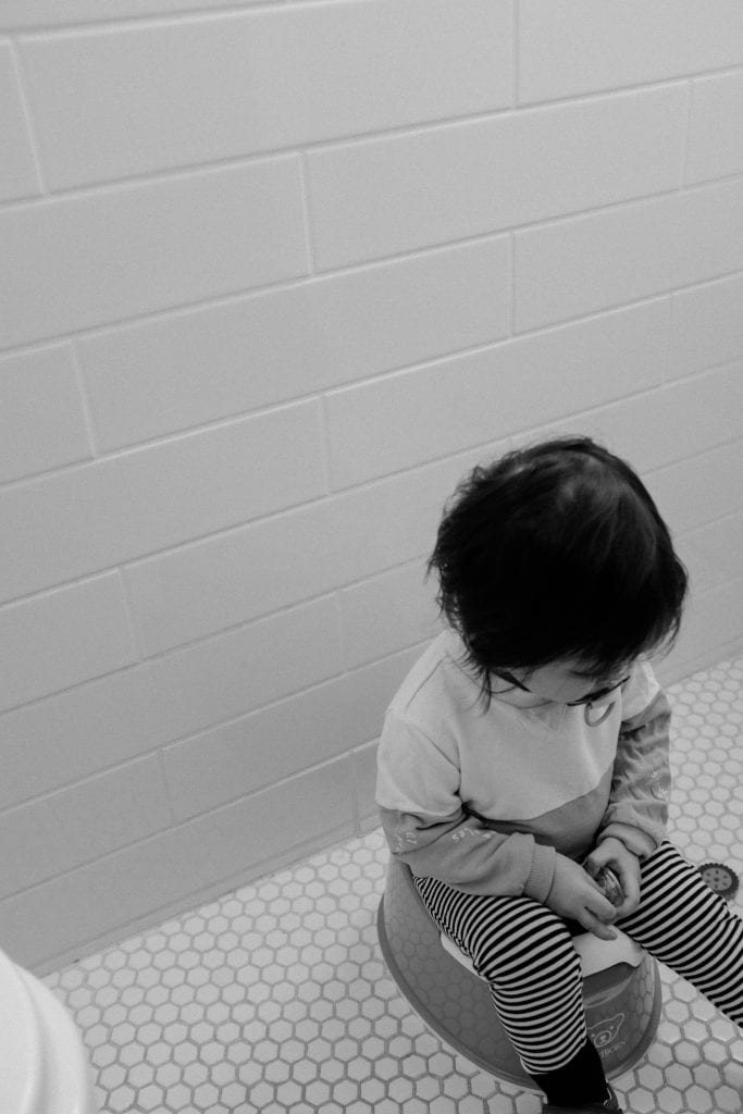 toddler sitting on a child's potty seat in a tiled room