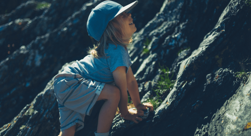 boy with a blue hat climbing a rocky hill