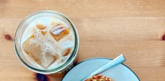 Viewed from above, an iced coffee next to a plate with oat milk blueberry muffin square