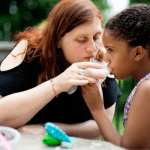 mother helps daughter hold a cup