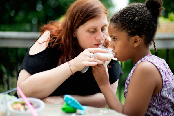 mother helps daughter hold a cup with a beverage. The child appears to be about 9 years old.