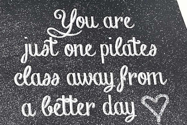 Cursive writing on a chalkboard that says "You are one Pilates class away from a better day."