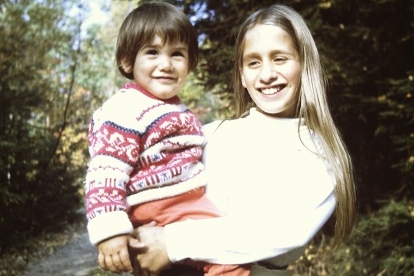 A teenaged girl holds a toddler on a wooded path.