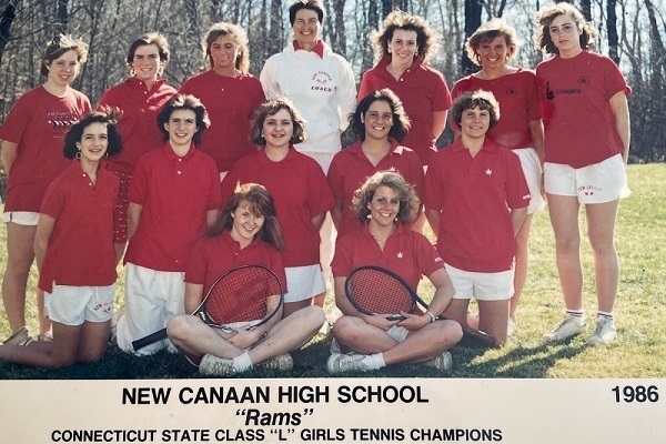 A team of girls who play tennis, dressed in red shirts and white shorts, posing for a picture.