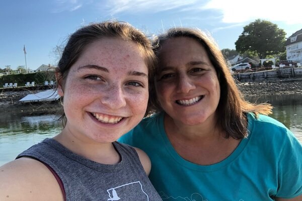 A mother and daughter pose for a photo along a rocky seashore.