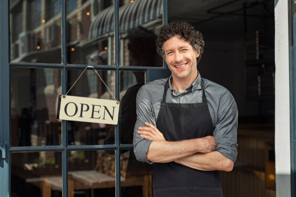 man in an apron in front of a restaurant "open" sign